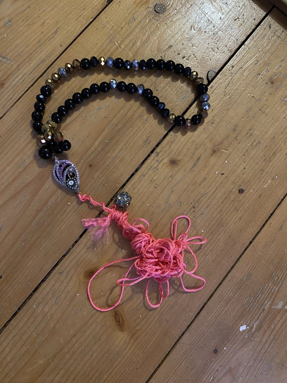 Black and gold beaded Eye assemblage with loose bright pink thread on a wooden work surface